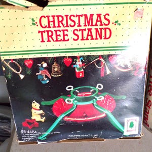 May include: A red and green Christmas tree stand with a metal base and four arms. The box reads "Christmas Tree Stand" and "For trees up to 7 ft. tall".