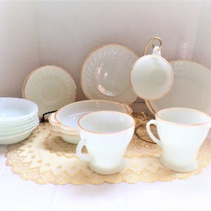 Op de afbeelding: Een set vintage melkglas servies in een lichtgroene kleur met gouden rand. De set bevat een roomkan, suikerpot, theekopje en schoteltje, en verschillende kommen.