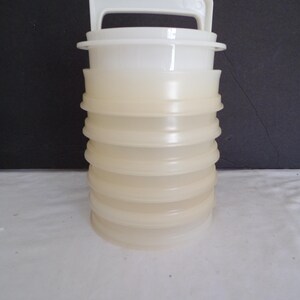 May include: A set of white plastic stackable containers with a handle on the top. The containers are translucent and have a slightly yellowed hue.
