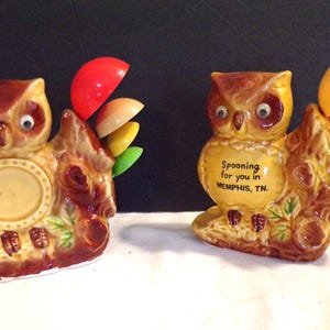 Könnte beinhalten: Zwei Keramik-Eulenfiguren in Braun und Gelb, die auf einem Baumstamm-Sockel sitzen. Eine Eule hat ein kreisförmiges Design, die andere hat den Text "Spooning for you in Memphis, TN." Jede hat farbenfrohe löffelförmige Akzente.