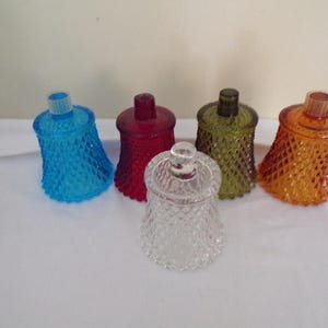 May include: Five glass candle holders in various colours, including blue, red, green, orange, and clear. The holders have a textured, diamond-like pattern.