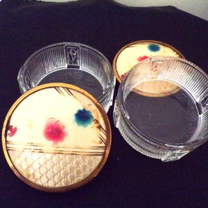 May include: A vintage glass and metal three-tiered trinket box with a floral design on the lid. The box is clear glass with a gold rim and a white base with painted flowers in red, blue, and green.