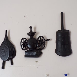 May include: Three black decorative wall ornaments featuring a fireplace bellows, a vintage coffee grinder with side wheels, and a wooden butter churn. Each piece is molded with detailed textures and relief patterns, finished in a solid matte black.