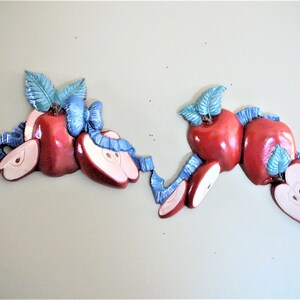 May include: A set of two wall decorations featuring red apples with green leaves and blue ribbon accents. The apples are arranged in a cluster, with some cut in half to reveal the inside.