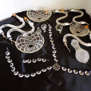 May include: A set of crystal chandelier parts, including glass shades, crystal drops, and metal arms. The parts are arranged on a black fabric surface.