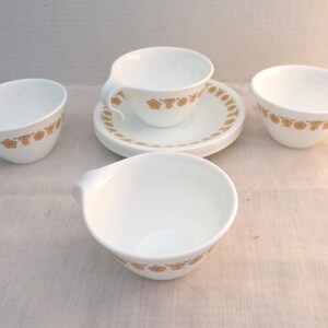 Può includere: Set di quattro tazze da tè in ceramica bianca con un motivo floreale dorato. Le tazze hanno un design di manico unico e sono perfette per servire tè o caffè.