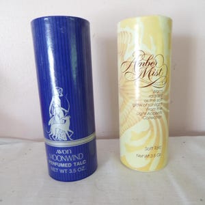 May include: Two cylindrical containers of perfumed talc. The blue container is labelled Avon Moonwind Perfumed Talc Net Wt 3.5 oz and features a silver illustration of a figure with a dog. The yellow container is labelled Amber Mist Soft Talc Net Wt 3.5 oz.