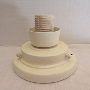 Pode incluir: Um candeeiro de teto branco com uma base redonda e uma tomada de plástico branca. O candeeiro tem duas pequenas maçanetas no lado.