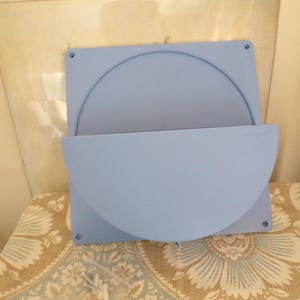 May include: A light blue wall-mounted planter with a semi-circular design. The planter is made of plastic and has a smooth surface.
