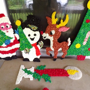 May include: A collection of vintage Christmas decorations, including Santa Claus, a snowman, a reindeer, and a Christmas tree. The figures are made of textured, colorful plastic and are arranged on a table.