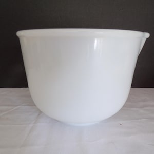 Pode incluir: Uma tigela branca para misturar com base arredondada e bico. A tigela é feita de um material brilhante e tem uma superfície lisa e limpa. O fundo é de cor escura e a tigela está sobre uma superfície branca.