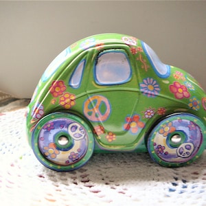 Può includere: Un'auto giocattolo verde con un simbolo di pace e disegni di fiori. L'auto ha un parabrezza blu e ruote viola, verdi e gialle.