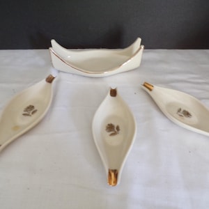 以下が含まれることがあります： ヴィンテージのクリーム色のセラミック灰皿と、それに合うホルダーのセット。灰皿は葉の形で、金色のアクセントと花の模様があります。ホルダーはボート型で、金色のトリムが付いています。