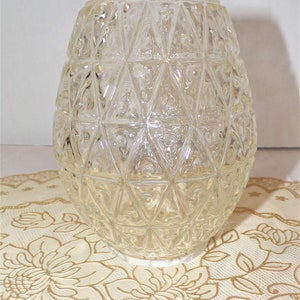 May include: A clear glass vase with a geometric pattern. The vase has a round shape and is made of thick glass.