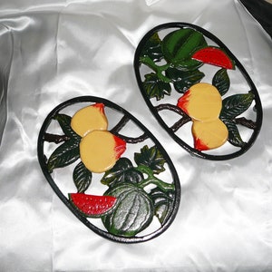 Puede incluir: Dos posavasos de hierro fundido negro con un diseño de fruta. Un posavasos presenta una sandía y melocotones, el otro presenta una sandía y melocotones.