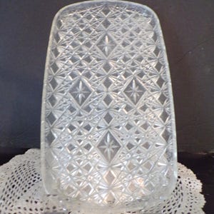 May include: A rectangular clear glass tray featuring a pressed diamond and starburst pattern across its entire surface. The tray has rounded corners and a raised edge, showcasing a geometric design that reflects light through the glass.