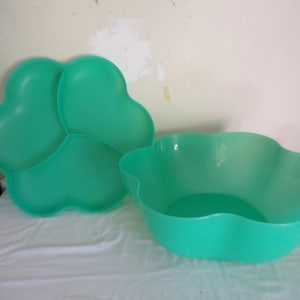 May include: A set of two teal-colored plastic serving dishes. One is a three-sectioned clover-shaped tray, and the other is a matching scalloped-edge bowl. The dishes are made of a durable plastic material.