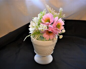 May include: A white milk glass vase with a textured design holds a bouquet of pink and white artificial flowers.