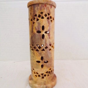 May include: A carved stone incense burner with a decorative pattern. The burner is a light brown color with hints of pink and white.