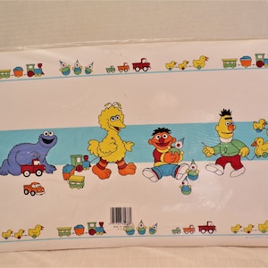 May include: A Sesame Street themed placemat featuring Big Bird, Cookie Monster, Elmo, and Bert. The placemat has a blue and white border with a repeating pattern of toy trains, trucks, and ducks. The placemat is made of a durable material and is perfect for kids.