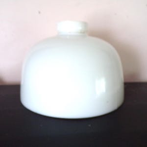 May include: A dome-shaped white glass lamp shade with a smooth, opaque finish. The shade features a circular opening at the top with a raised collar, designed for attachment to a light fixture. The overall form is rounded and symmetrical.