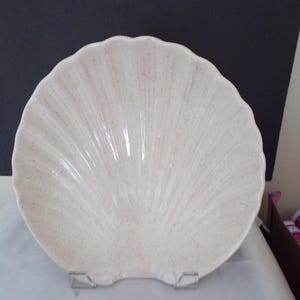 May include: A white ceramic serving dish shaped like a seashell with a speckled texture.