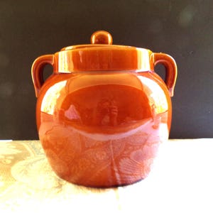 May include: A brown ceramic crock pot with a lid. The crock pot has two handles and a rounded body.