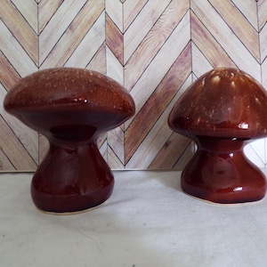 Puede incluir: Dos saleros y pimenteros de cerámica marrón en forma de hongo. Los saleros tienen un acabado brillante y un esmalte marrón claro.