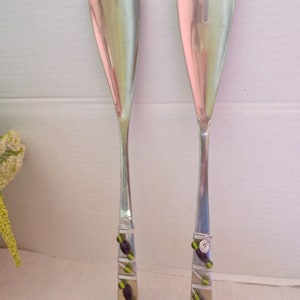 May include: A set of two silver salad servers with green and purple beads wrapped around the handles.