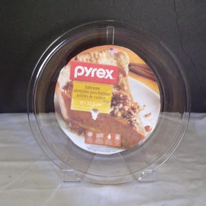 Puede incluir: Fuente para tarta Pyrex transparente, de 22,5 cm de diámetro, sobre un soporte transparente. La fuente tiene una etiqueta con el logotipo de Pyrex y una imagen de una tarta. La etiqueta también incluye las palabras "bakeware utensils para hornear articles de cuisson".