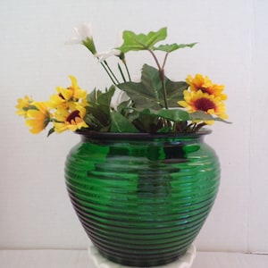 May include: A green glass vase with a ribbed design, filled with yellow and white artificial flowers.