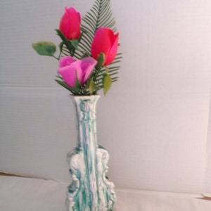 May include: A green and white ceramic vase shaped like a violin with three pink and red artificial roses.