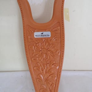 May include: A tan-colored boot jack with a floral design and the text "Western Express, Inc." The boot jack is made of a durable material and features a decorative embossed pattern. The design includes a large flower and scrolling leaves.