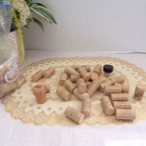 May include: A close-up of a pile of natural cork wine bottle stoppers on a white lace doily. The corks are various sizes and shapes, some with the brand name "Gallo Family Vineyards" printed on them.
