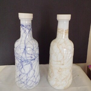 May include: Two glass bottles with white lids and a swirled design. One bottle has blue swirls and the other has brown swirls.