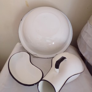Puede incluir: Un juego de tres artículos de baño de esmalte blanco con ribete negro. El juego incluye un tazón grande, un plato en forma de riñón y una jarra con asa.