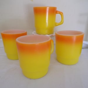 May include: Four vintage glass mugs with a yellow to orange gradient. Two mugs have handles, and two are handleless. The mugs have a retro design and are likely from the mid-century era. The mugs are made of glass.