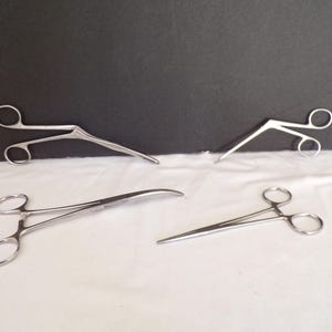 Puede incluir: Cuatro pinzas médicas de acero inoxidable con puntas curvas. Las pinzas están dispuestas sobre una superficie blanca.