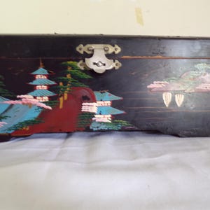 以下が含まれることがあります： 黒い木製の箱で、蝶番式の蓋と金属製の留め金が付いています。 箱は、塔、木、山々を特徴とするカラフルな風景シーンで装飾されています。 アートワークは、青、赤、緑、ピンクの色合いで塗装されています。