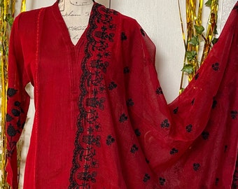 Puede incluir: Un vestido rojo bordado con diseños florales negros. El vestido tiene mangas largas y un escote en V. La tela es transparente y tiene una textura delicada.