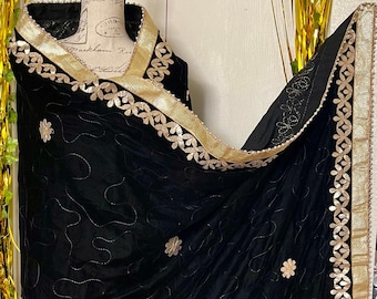 May include: Black velvet shawl with gold floral trim and embroidered details. The shawl has a scalloped edge with gold accents and delicate floral embroidery. A luxurious accessory for special occasions.