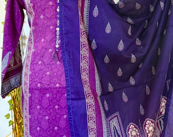 May include: A two-piece purple and blue salwar kameez set. The long-sleeved tunic is a vibrant purple with a floral pattern, and the matching scarf is a deep blue with a paisley design. The set features intricate detailing and a tassel.