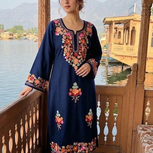May include: A navy blue long-sleeved tunic featuring a notched neckline and vibrant floral embroidery in shades of orange, pink, and green. The embroidery patterns are concentrated around the neckline, cuffs, and lower hem, with additional floral motifs.