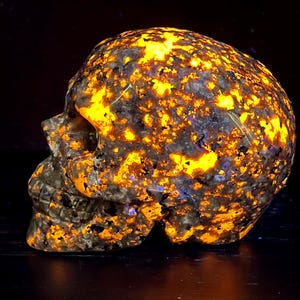May include: A skull-shaped sculpture carved from a dark, speckled stone with a bright orange glow. The stone is full of small, bright orange flecks.