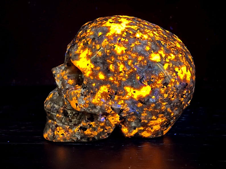 May include: A skull-shaped sculpture carved from a dark, speckled stone with a bright orange glow. The stone is full of small, bright orange flecks.