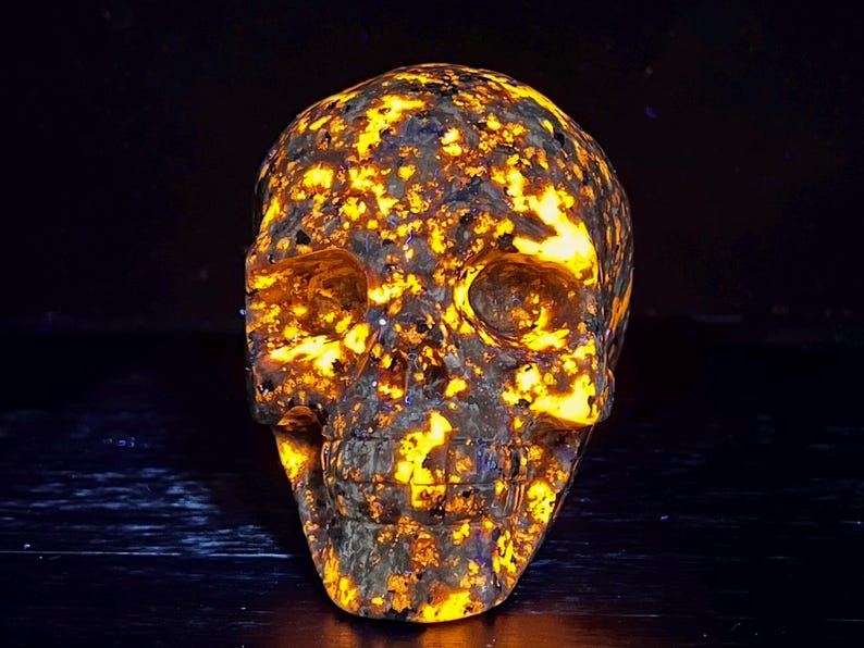 May include: A skull carved from a yellow and black speckled stone, glowing under a black light.