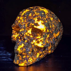 May include: A skull carved from a yellow and brown stone with a speckled pattern. The skull glows under a black light, revealing a bright yellow and orange pattern.