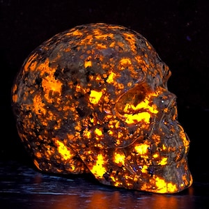 May include: A skull-shaped rock with a dark brown exterior and a bright orange glow emanating from the inside. The rock is covered in small, orange-colored crystals.