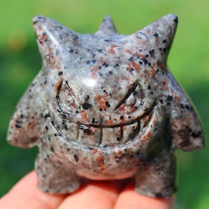 Puede incluir: Una talla de piedra gris, negra y roja moteada de un fantasma de dibujos animados con una amplia sonrisa de dientes.