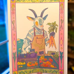 May include: A colorful illustration of a goat-like character in an apron, holding carrots at a farmer's market. The artwork features crates of produce, including pumpkins and eggplants, with a decorative border of vegetables and stars. The artist's name, KAYCAT, is in the bottom right corner.